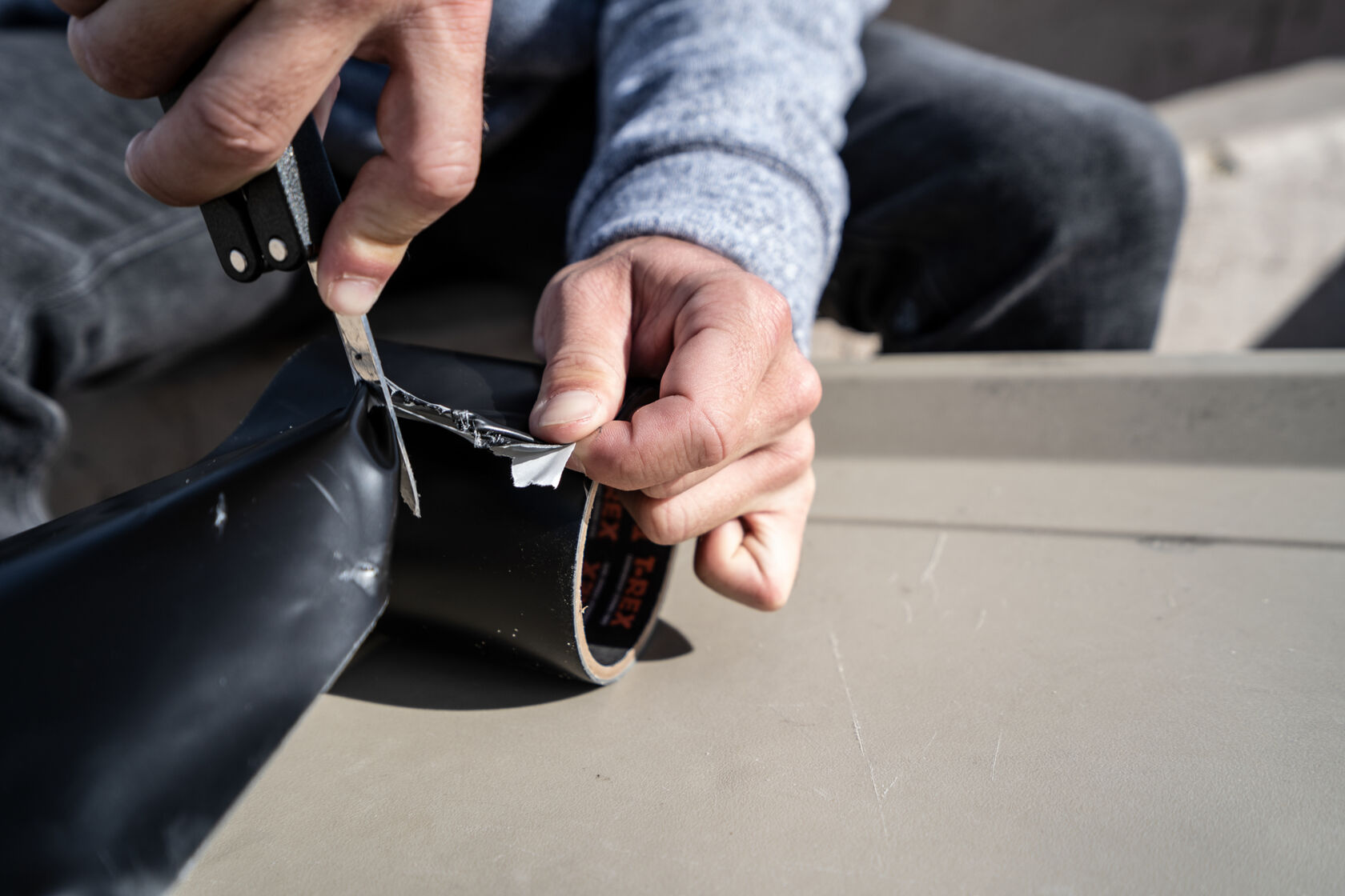 Man cutting a roll of T-Rex Extreme Strength Waterproof and Repair Tape to repair a boat leak