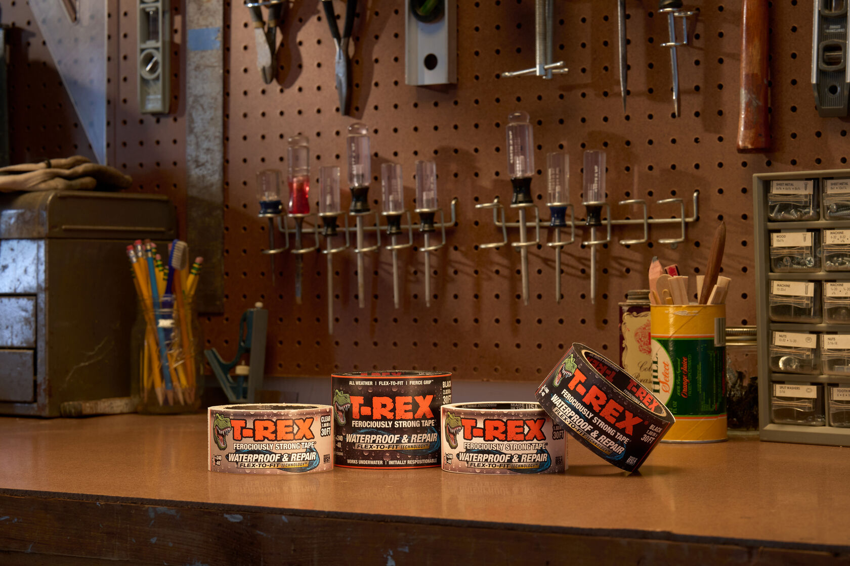 4 rolls of T-Rex Ferociously Strong Waterproof and Repair Tape on a work bench. Clear, Black, White, and Black