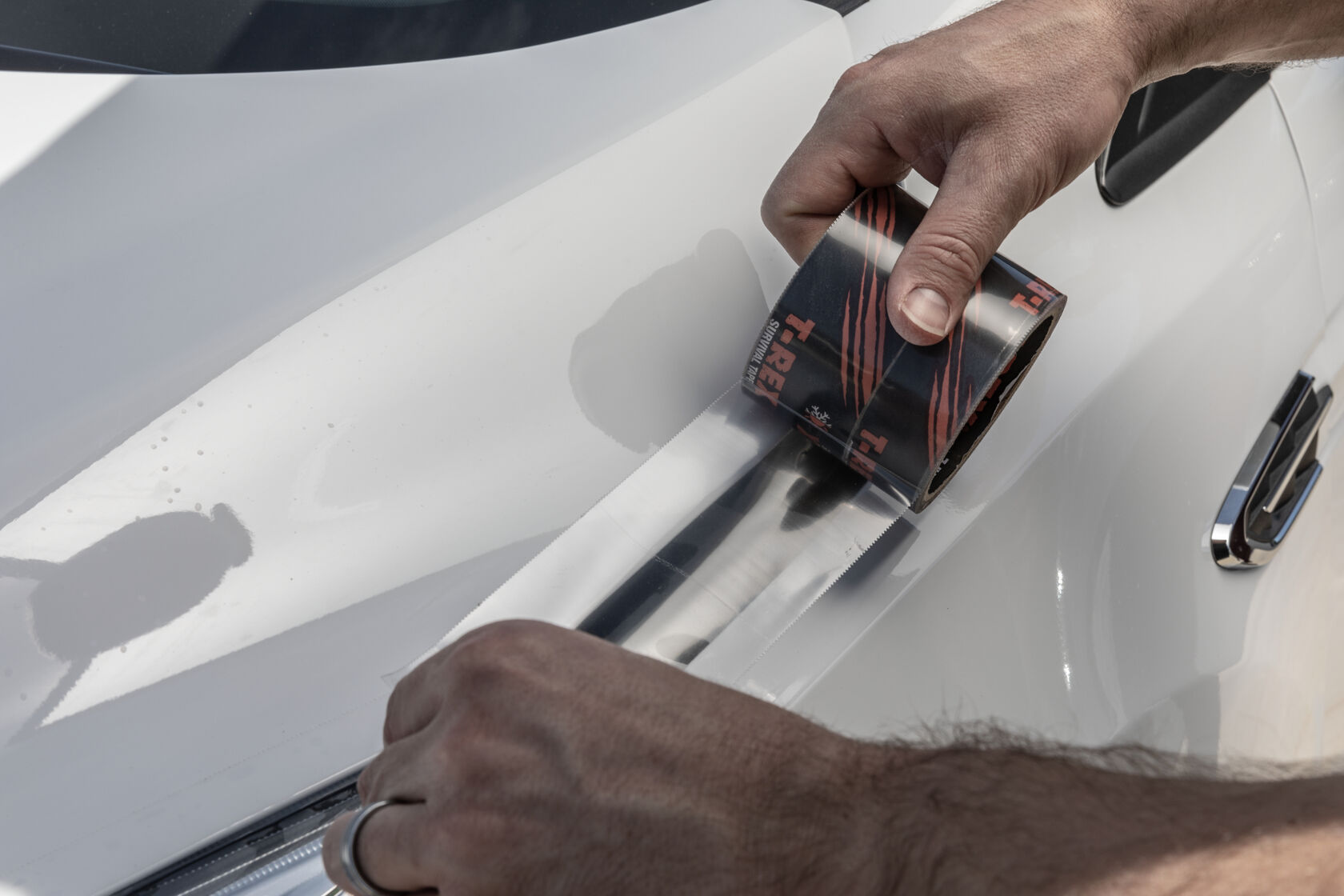 A man repairing his car headlight with a roll of T-Rex Clear Repair Tape